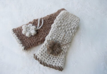Gehäkelte, fingerlose Armstulpen in Beige und Braun mit Blumenapplikationen auf hellem Untergrund