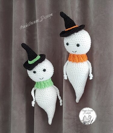 Zwei gehäkelte weiße Geister mit schwarzen Hexenhüten und grüner sowie orangener Halskrause