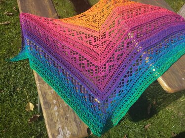 Gehäkeltes Dreieckstuch in Regenbogenfarben mit Lochspitzenmuster auf einer Holzbank