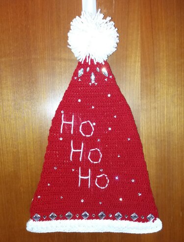 Rote gehäkelte Weihnachtsmütze mit weißem Bommel, besticktem HO HO HO und Strasssteinen an Holztür hängend