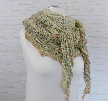 Gehäkeltes Dreieckstuch in melierten Pastell- und Naturtönen auf einer Schneiderpuppe vor heller Ziegelwand