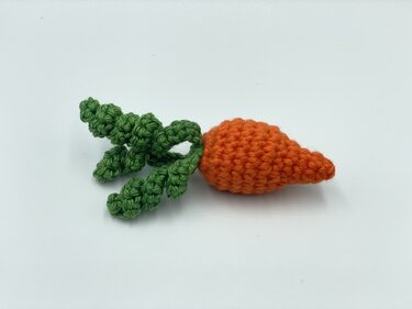 Gehäkelte orange Karotte mit grünen krausen Blättern auf weißem Hintergrund.