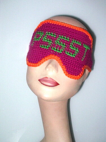 Gehäkelte Schlafmaske in Magenta mit grünem Schriftzug „PSSST“ und orangefarbener Umrandung auf Mannequin.