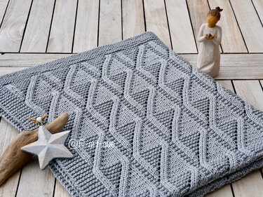 Folded light-gray knitted baby blanket showing repeating diamond texture and garter-stitch border on pale wooden surface