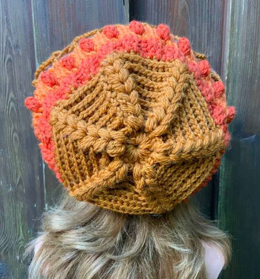 Rückansicht einer Person mit gehäkelter Mütze in Braun und Orange mit Noppen- und Zopfmustern.