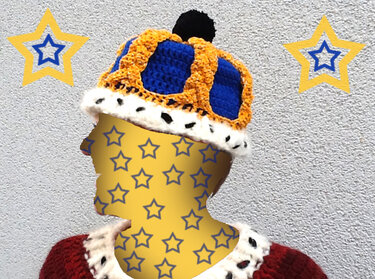 Modell mit gehäkelter Kronen-Mütze in Blau und Gelb, mit weißem gepunktetem Rand und schwarzem Bommel