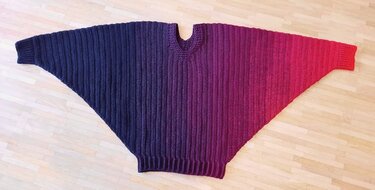 Gehäkelter breiter Poncho mit V-Ausschnitt und Farbverlauf von Violett zu Rot auf hellem Holzboden
