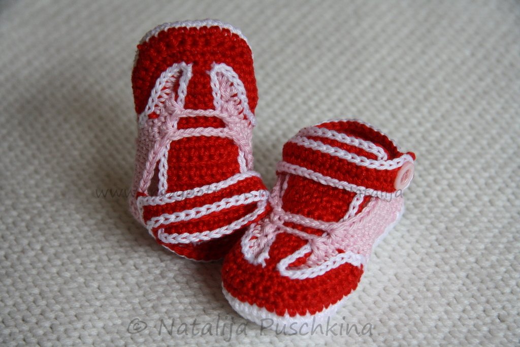 Gehäkelte Babyschuhe in Rot, Rosa und Weiß im Sneaker-Look auf heller Strickunterlage