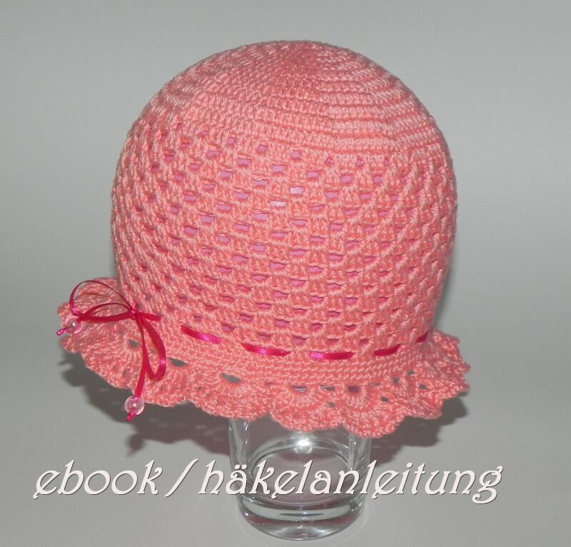rosafarbene gehäkelte Mütze mit gezacktem Rand und pinkem Band auf Glasständer