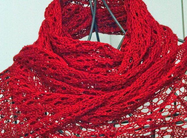 Tiefrotes, gestricktes Lacetuch mit filigranem Lochmuster, locker drapiert an einem Drahtgestell.