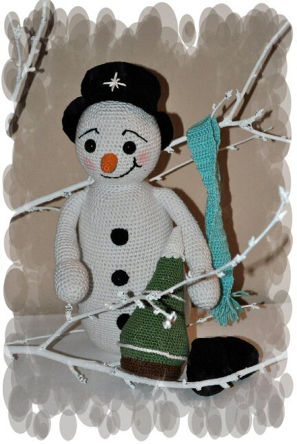 Gehäkelter Schneemann-Amigurumi mit schwarzem Zylinder, orangefarbener Nase, türkisfarbenem Schal und kleinem grünen Baum