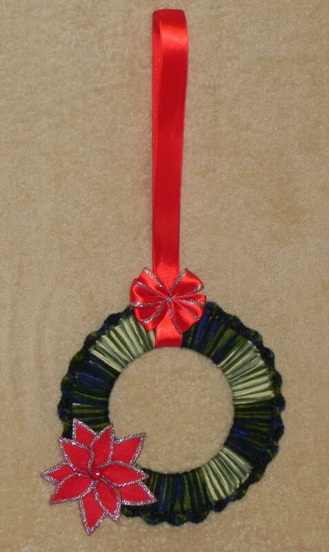Handgehäkelter Weihnachtskranz in Grün und Blau mit rotem Weihnachtsstern und roter Satinschleife.