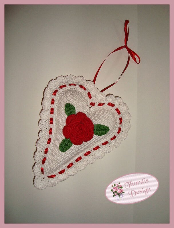 Gehäkeltes weißes Herz mit roter Rosen‑Applikation, grünen Blättern und rotem Band