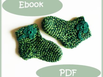 Zwei grüne gehäkelte Babysocken mit dunkelgrünen Kleeblatt-Applikationen auf weißem Hintergrund