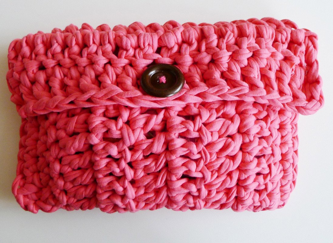 Pinkfarbene gehäkelte Clutch mit rundem braunem Knopf auf hellem Hintergrund