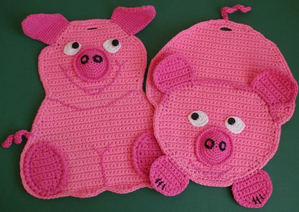 Zwei rosa gehäkelte Topflappen in Schweineform auf grünem Hintergrund