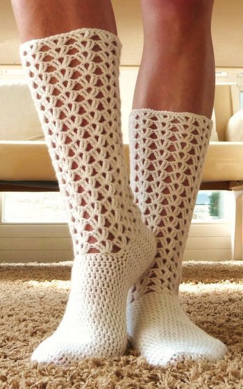 Beine in cremefarbenen, gehäkelten Kniestrümpfen mit offenem Spitzenmuster und geschlossenem Fußteil
