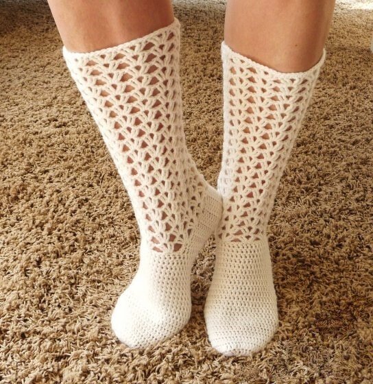 Weiße gehäkelte wadenhohe Socken mit feinem Lochmuster auf hellem Teppich.