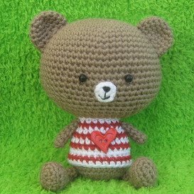 Brown crocheted amigurumi teddy bear wearing a red-and-white striped shirt with a red heart applique.