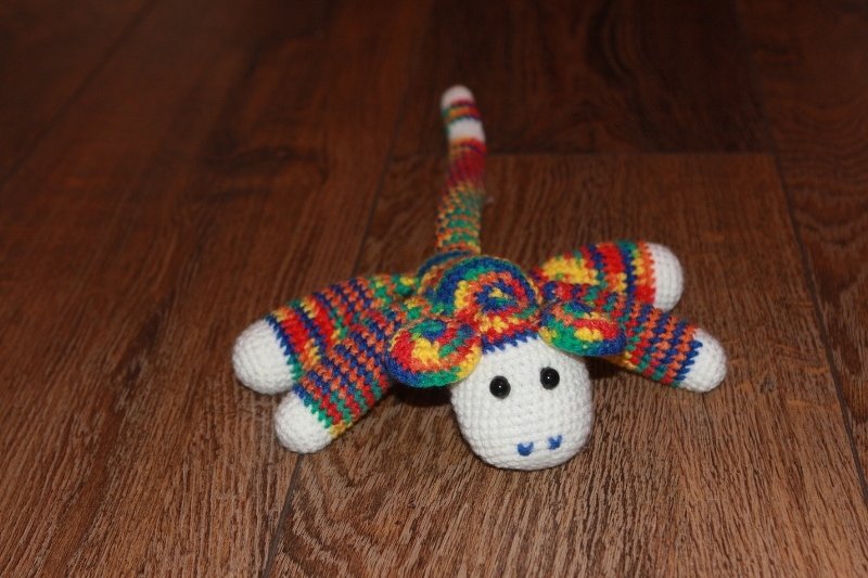 Gehäkelter Amigurumi-Affe mit weißem Gesicht und buntem Streifenmuster auf Holzboden