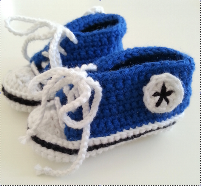 Ein Paar blau-weiße gehäkelte Babyschuhe mit Schnürsenkeln und seitlichem Stern‑Patch.