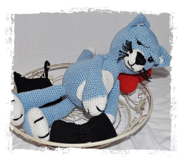 Gehäkelte blaue Amigurumi-Katze mit weißen Pfoten und rotem Herz in Metallschale