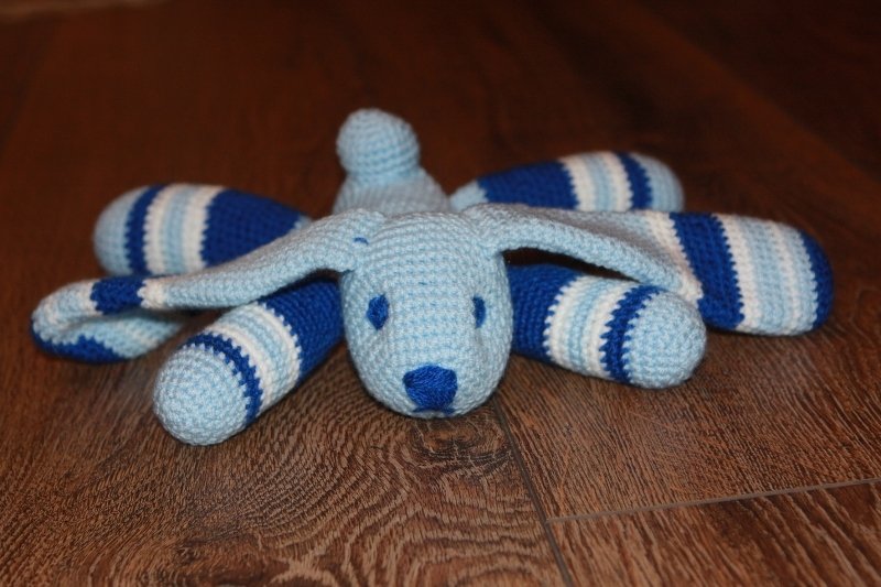 Handgearbeitet wirkender Amigurumi-Hase mit blauen Streifen und langen Ohren auf Holzboden