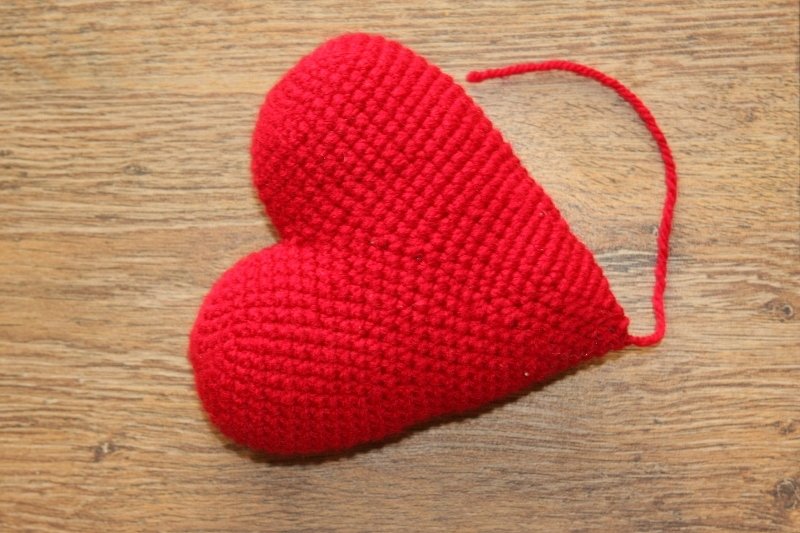 Rotes gehäkeltes Amigurumi-Herz mit sichtbarer Maschenstruktur und losem Faden auf Holz
