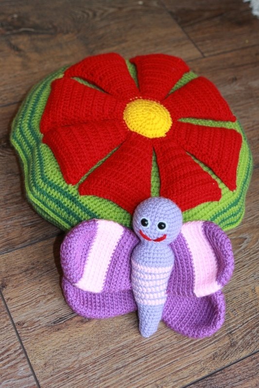 Rundes gehäkeltes Kissen mit roter Blume und lila Schmetterling davor
