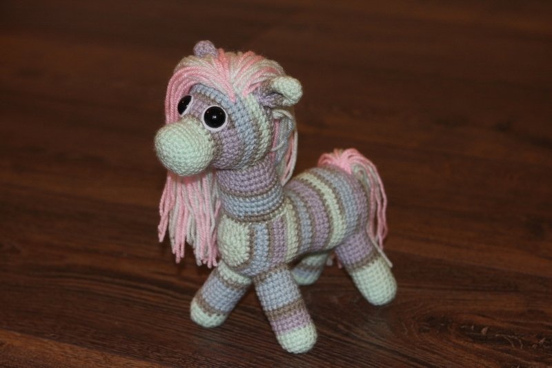 Gehäkeltes Amigurumi-Pony mit rosa Mähne und pastellgestreiftem Körper