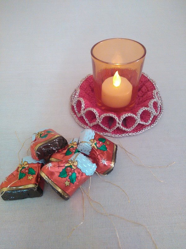 Roter gehäkelter Untersetzer mit silberner Borte, Glas mit Teelicht und weihnachtlich verpackte Süßigkeiten daneben