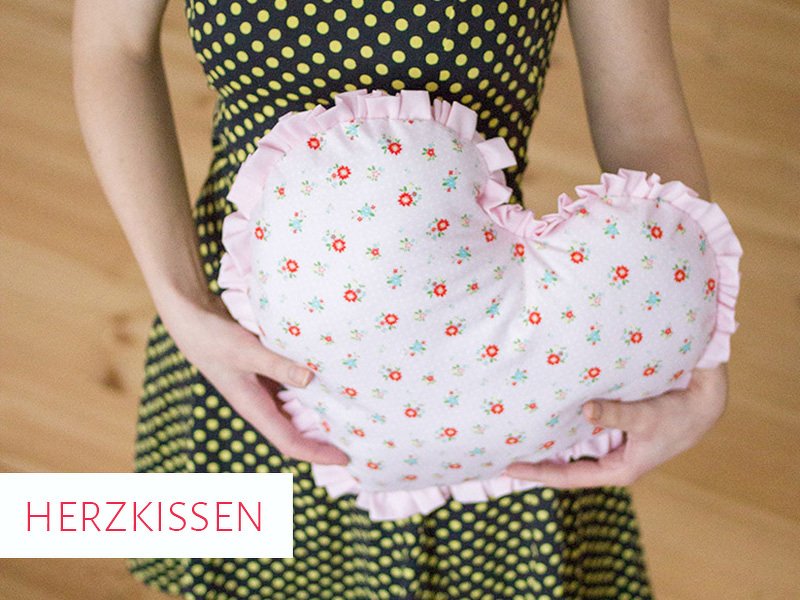 Eine Person hält ein rosa Herzkissen mit Blumenmuster und Rüschen.