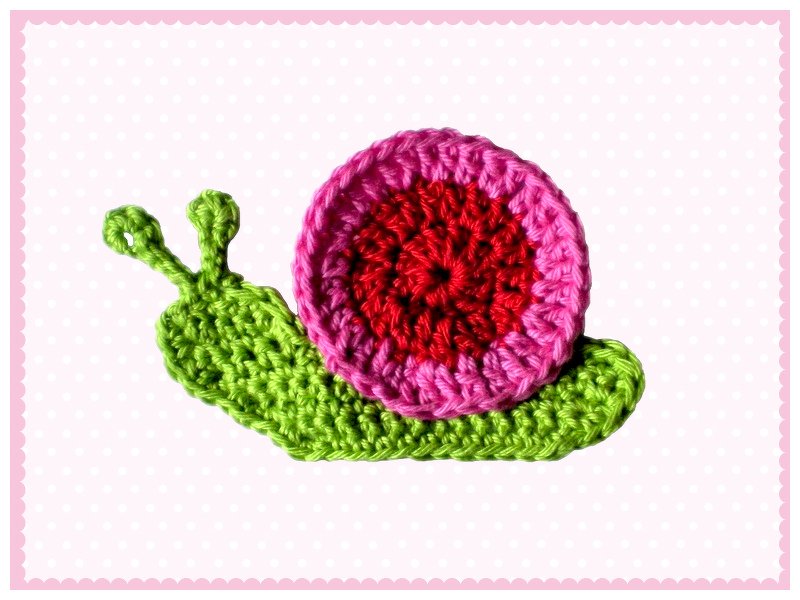 Compact green crochet snail appliqué with red and pink shell on pale polka-dot surface