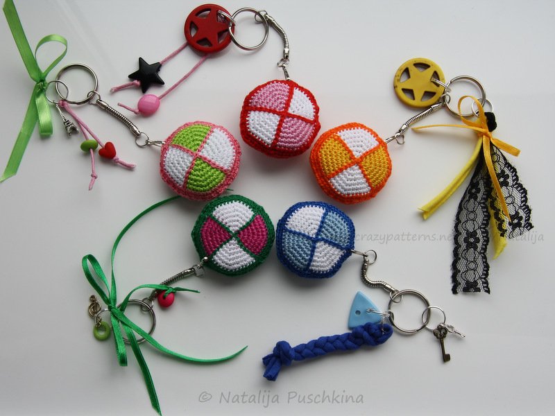 Bunte gehäkelte Kugel-Schlüsselanhänger mit Bändern und Charms auf weißem Hintergrund