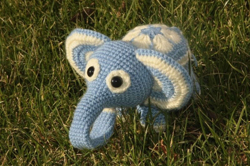 Handgehäkelter Elefant in Hellblau und Creme auf grünem Gras.