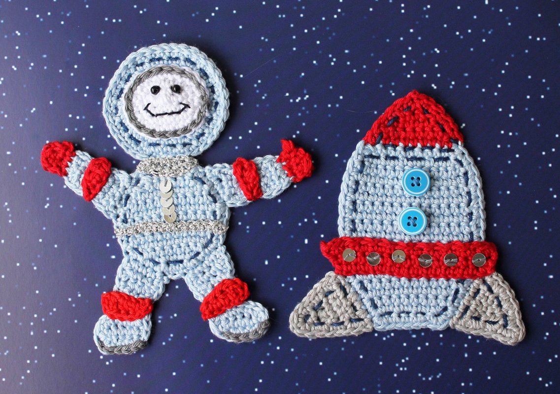 Gehäkelter Astronaut und Rakete als Applikationen auf dunkelblauem Sternenhintergrund