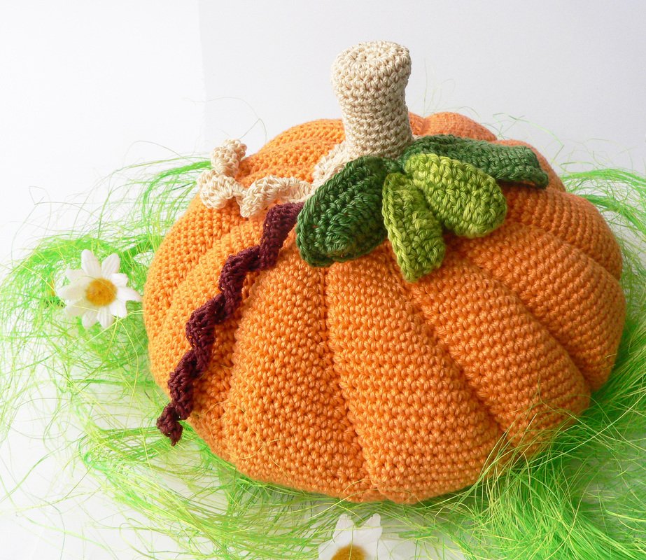 orange crocheted pumpkin plush with beige stem and green leaves on green raffia