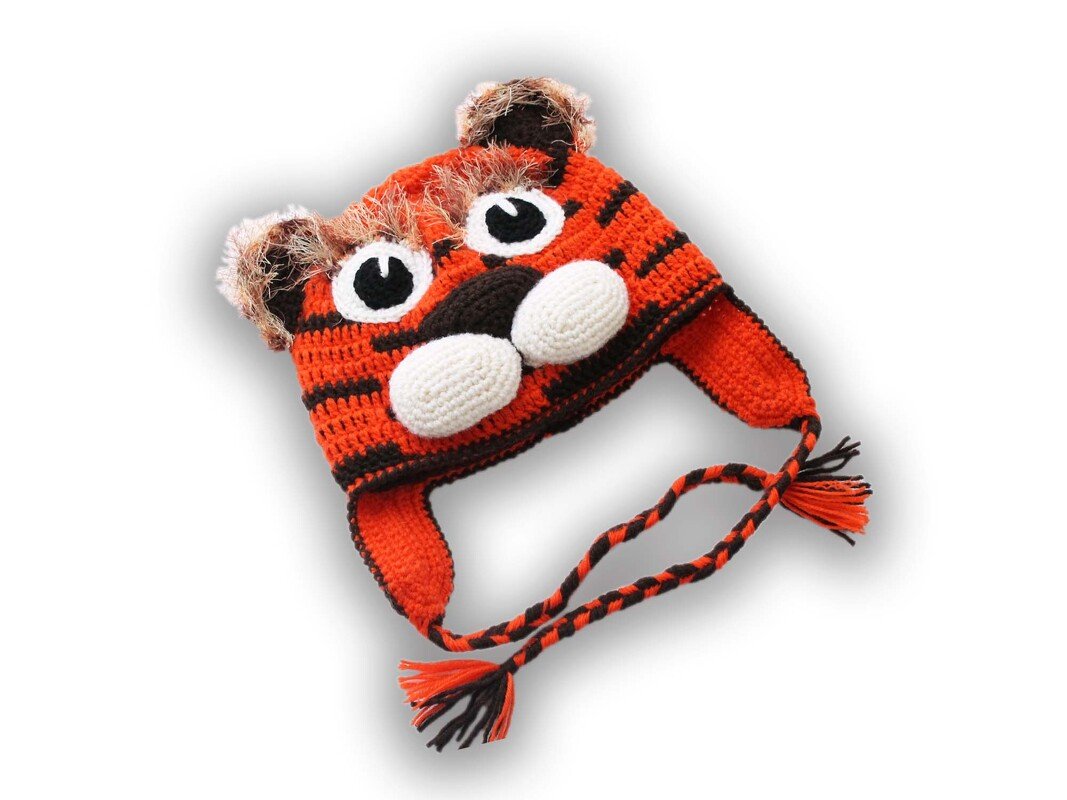 Gehäkelte Tigermütze mit orange-schwarzen Streifen, weißen Augen, schwarzer Nase und geflochtenen Ohrenklappen