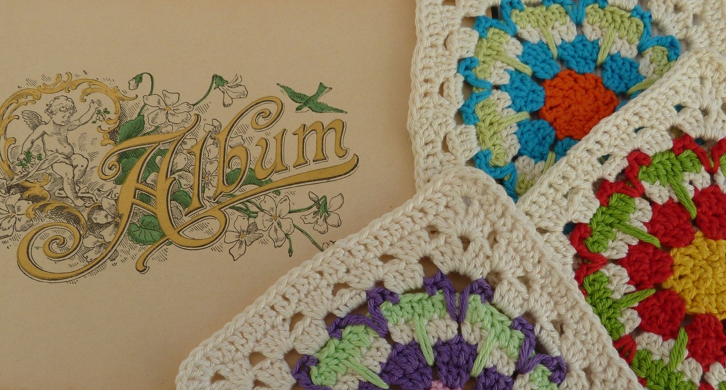 Mehrere bunte gehäkelte Granny-Squares mit cremefarbener Umrandung neben einer alten Albumseite mit floraler Verzierung und dem Schriftzug "Album".