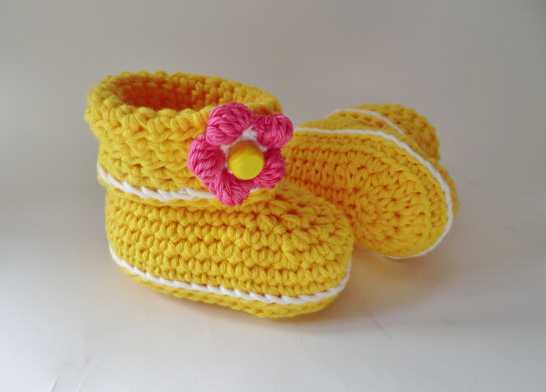 Gehäkelte gelbe Babyschuhe mit weißer Kante und rosa Blüte, Nahansicht