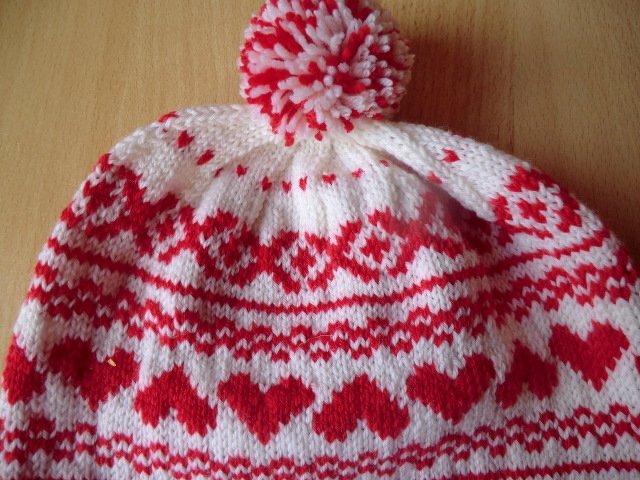 Weiß-rote gestrickte Kindermütze mit Herz- und Norwegermuster und Bommel