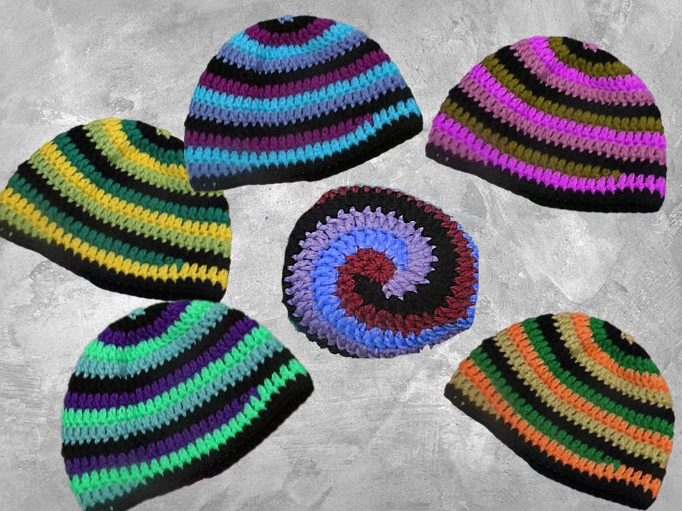 Mehrere gestreifte Häkelmützen in bunten Farben auf grauem Untergrund mit einem spiralförmigen Häkelstück.