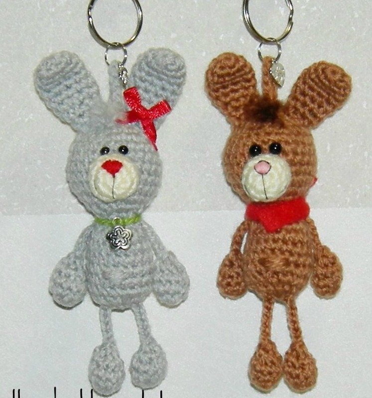 Zwei gehäkelte Amigurumi-Hasen-Schlüsselanhänger, grau mit roter Schleife und braun mit rotem Schal.