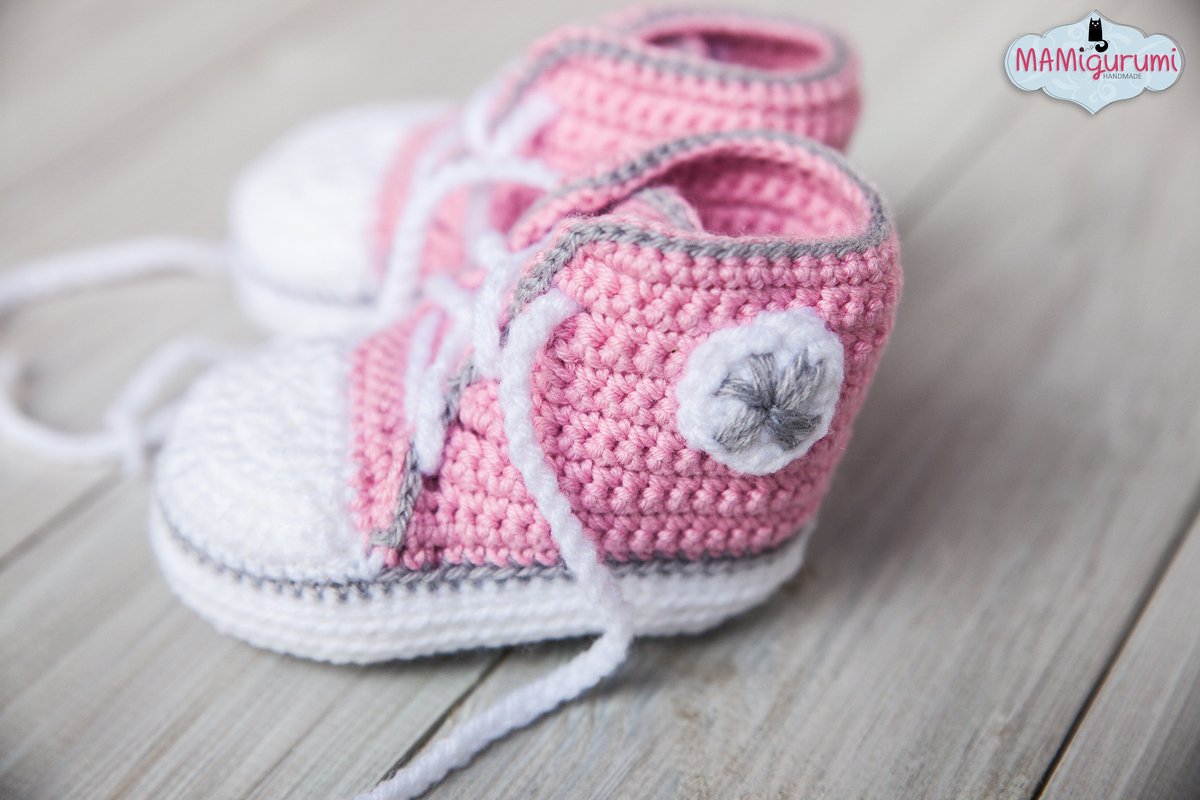 Gehäkelte Babysneaker in Rosa und Weiß mit weißen Schnürsenkeln auf heller Holzoberfläche