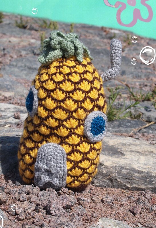 Gehäkeltes Ananas‑Häuschen Amigurumi mit grünem Blatt, runden Fenstern und seitlichem grauen Rohr