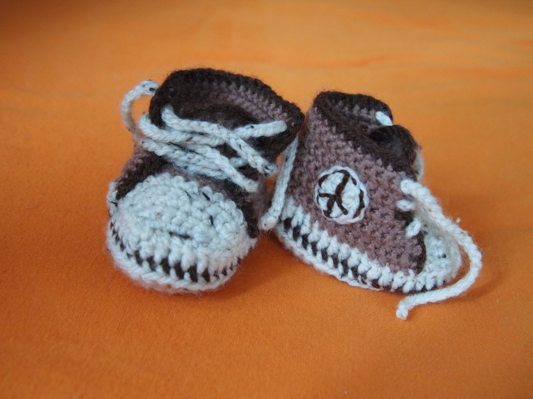 Nahaufnahme von gehäkelten Babyschuhen im Sneaker‑Design mit kontrastfarbener Kante