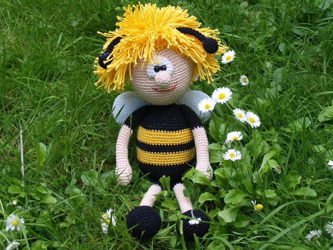 Gehäkeltes Bienen-Amigurumi mit gelben Haaren und kleinen Flügeln im Gras