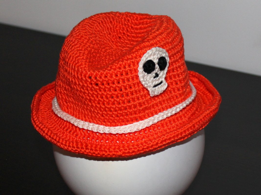 Leuchtend orange gehäkelte Babymütze mit weißer Kordel und Totenkopf-Applikation auf Modellkopf