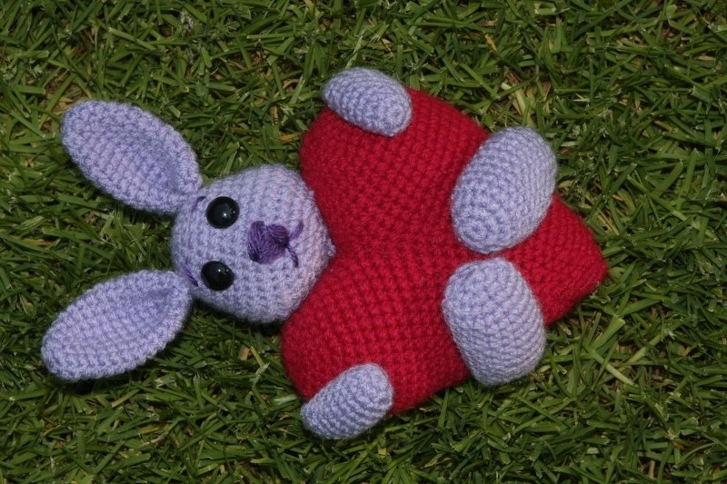 hellvioletter Amigurumi-Hase mit rotem Herz auf grünem Gras