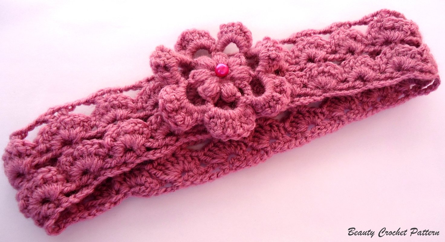 Rose-pink crocheted headband with layered flower and bead center on pale background